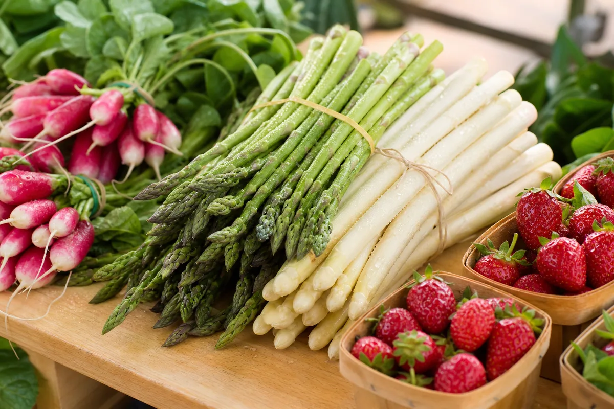 Étal de printemps avec bottes d’asperges, radis et premières fraises sur un marché de producteurs